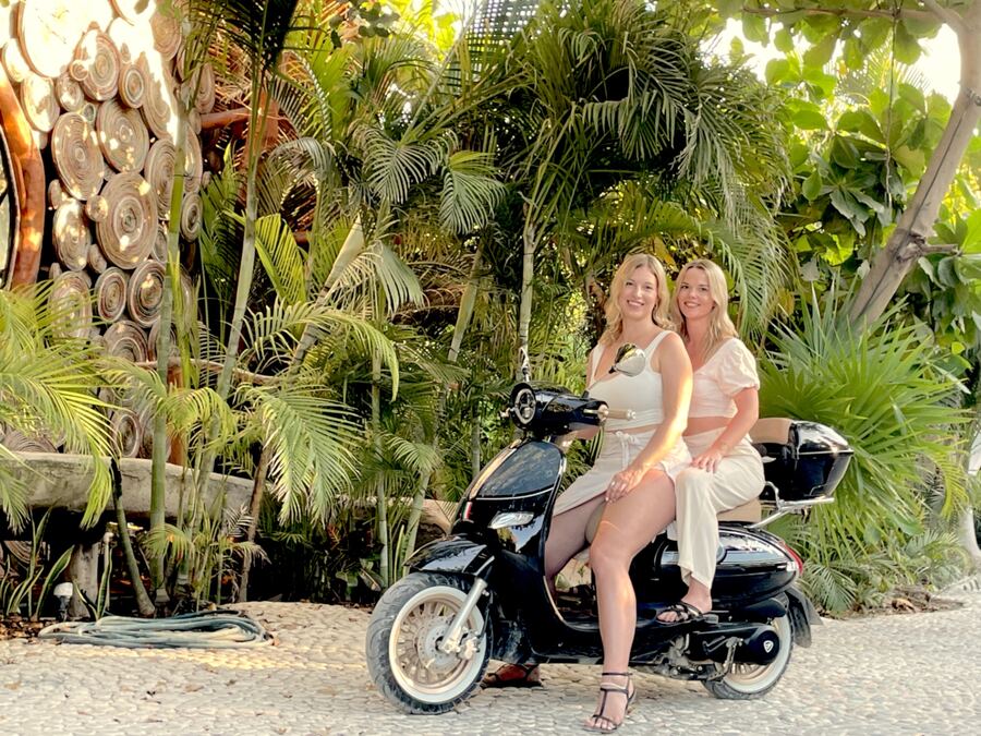 Two friends on a scooter surrounded by palms in Tulum